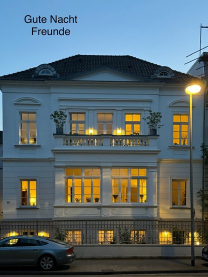 Abendansicht einer beleuchteten klassischen Gebäudefassade mit der Aufschrift 