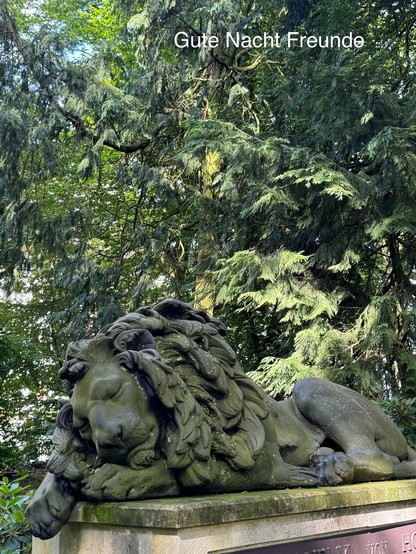 A moss-covered lion statue lies in a resting position against a backdrop of dense, green foliage. The text 