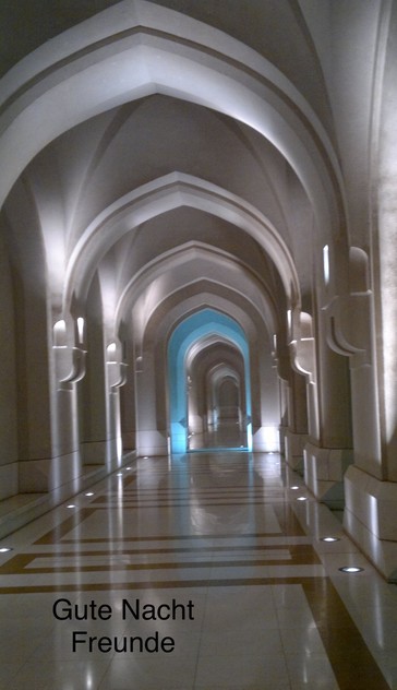 A well-lit, arched corridor with reflective flooring and intricate architectural design. Text at the bottom reads 