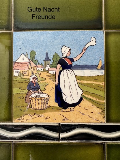 A tile artwork depicting a woman and a child in traditional attire, with the woman waving a cloth. Text above reads 