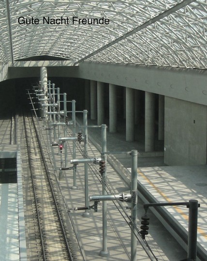 Train tracks inside a modern station with a lattice-style roof and text reading 