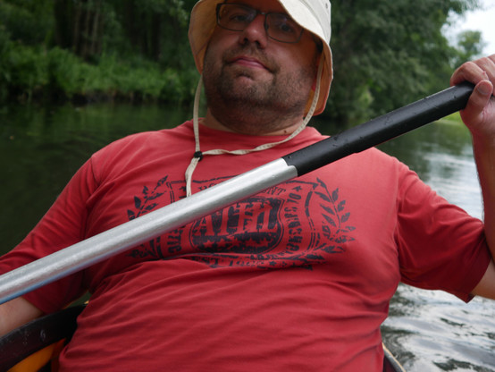 Foto von mir im Kanu beim Paddeln. Ich trage ein rotes T-Shirt und einen ziemlich albernen Sonnenhut in Beige.