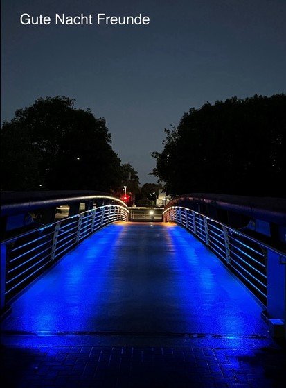 A pedestrian bridge illuminated with blue and orange lights at night. Text at the top says 