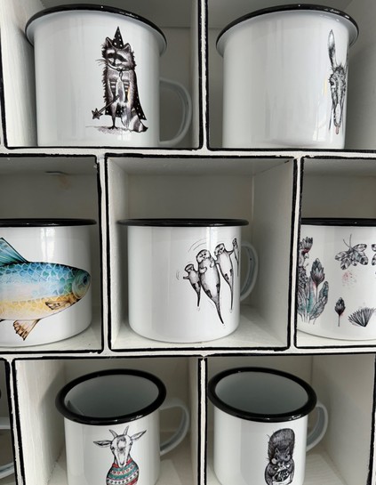A display of six white enamel mugs with black rims, each featuring a unique design, including animals and plants.

Ein Display von sechs weißen Emaille-Bechern mit schwarzen Felgen, die jeweils ein einzigartiges Design haben, einschließlich Tieren und Pflanzen.