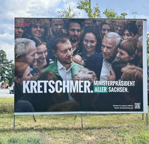 Riesiges Wahlwerbeplakat. In der Mitte Michael Kretschmer, umringt von Bürgern - Bild mutet an wie Adaption kirchlichen Motivs.