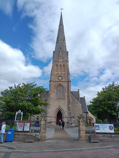 Kirche in Invergordon. Der Turm zur Straße beherbergt auch den Eingang. Die ganze Kirche ist aus einem gelblichen Gestein gebaut.
Der Kirchplatz ist komplett umzäunt, im Vordergrund ist der Eingang zu sehen.