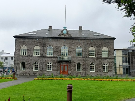 Parlamentsgebäude in Reykjavik.
Aus dunklem Gestein gebautes dreistöckiges Gebäude mit weißen Fenstern.