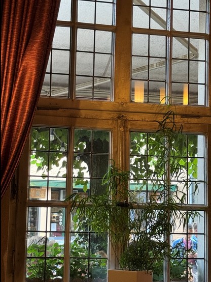 A window with multiple panes, partially covered by red curtains on the left. Green plants and tree are visible through the window, with some greenery placed inside on the windowsill.

Blick aus einem Gasthaus. Ein Fenster mit mehreren Scheiben, teilweise von roten Vorhängen auf der linken Seite bedeckt. Grüne Pflanzen und Bäume sind durch das Fenster sichtbar, wobei etwas Grün im Inneren auf der Fensterbank platziert ist.