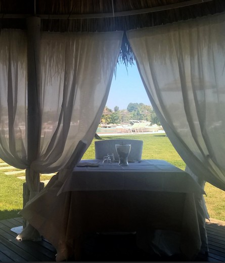 A table set for two inside a gazebo with white curtains, overlooking a grassy area with lounge chairs and a swimming pool in the background.

Ein Tisch für zwei Personen in einem Pavillon mit weißen Vorhängen, mit Blick auf eine grasbewachsene Fläche mit Liegestühlen und einem Swimmingpool im Hintergrund.