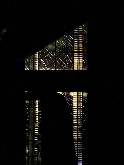 A dark image featuring a partial view of a window with art deco patterns, illuminated from behind. The shapes create an abstract design against the surrounding darkness.

Ein dunkles Bild mit einer Teilansicht eines Fensters mit dekorativen Art deco Mustern, das von hinten beleuchtet wird. Die Formen schaffen ein abstraktes Design gegen die umgebende Dunkelheit.