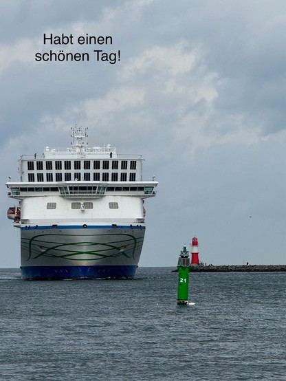 A large ship is approaching a harbor, with a green navigation buoy labeled 