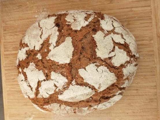 Ein braunes Brot mit unregelmäßigen Rissen in der Krume auf einem Holzbrett.