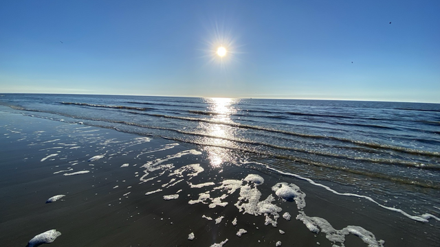 Die Sonne spiegelt sich im dunkelblauen Wasser der Nordsee, das am Strand von St. Peter Ording in ganz flachen Wellen ausläuft.