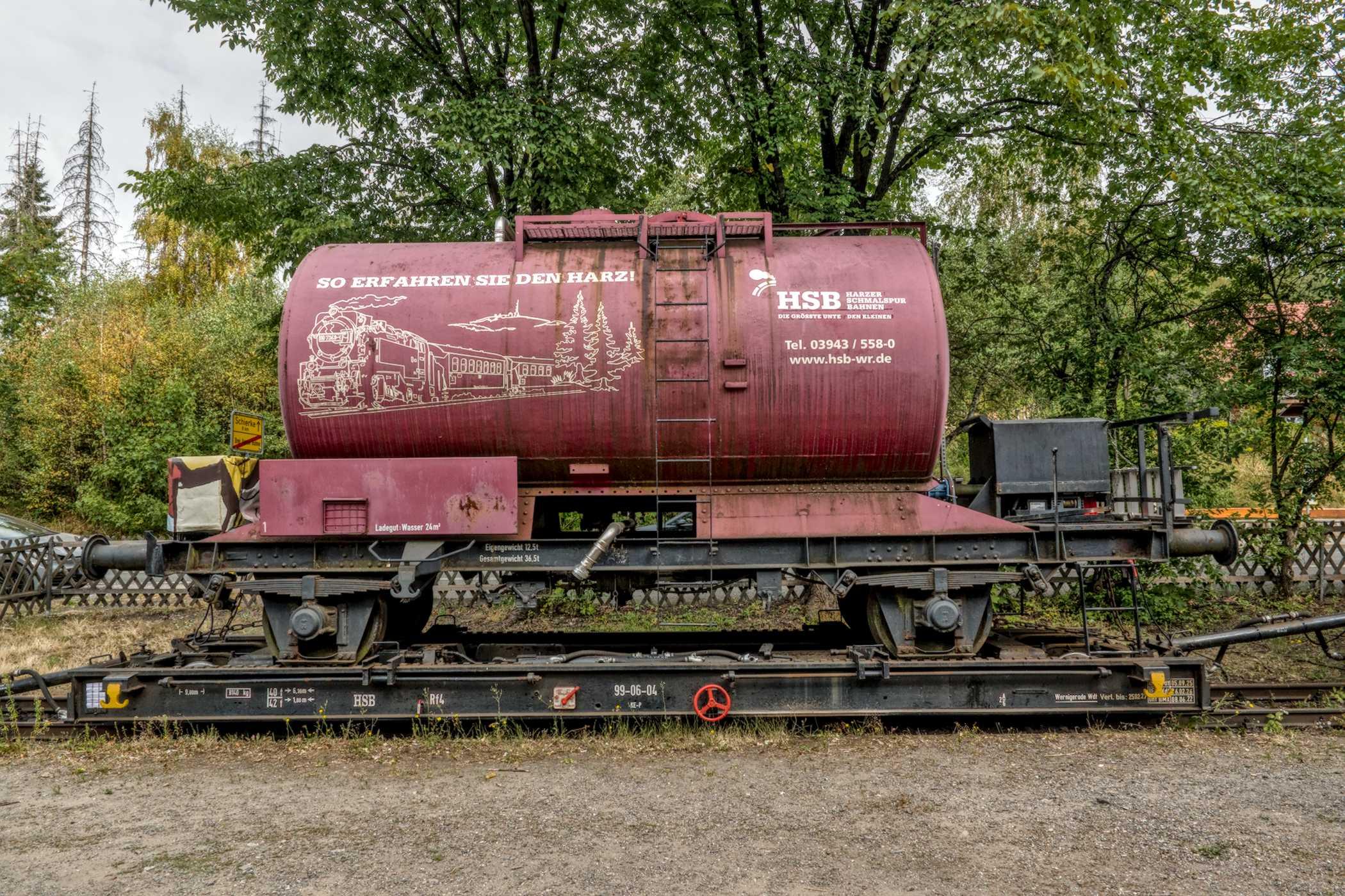 Farbfotografie im Format 3:2 Landscape.
Ein blassroter Tankwagen der Harzer Brockenbahn, steht, fest verankert, auf einem niederen Schwerlast-Fahrgestell. Er fasst 24 m³ Wasser, welche im Brandfall zur Brandstelle gefahren werden.