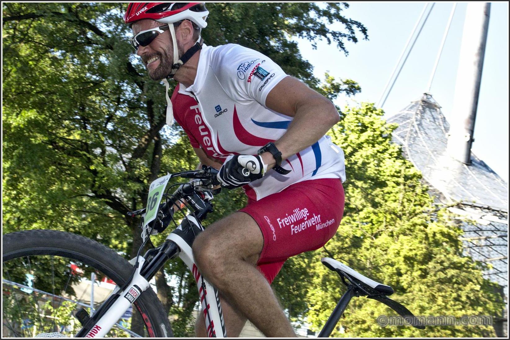 Farbfotografie im Format 3:2 Landscape.
Ein Tesmmitglied der Freiwilligen Feuwerwehr München, kämpft sich während eines 24h MTB Marathons auf dem Olympiagelände, eine steile Rampe hoch.